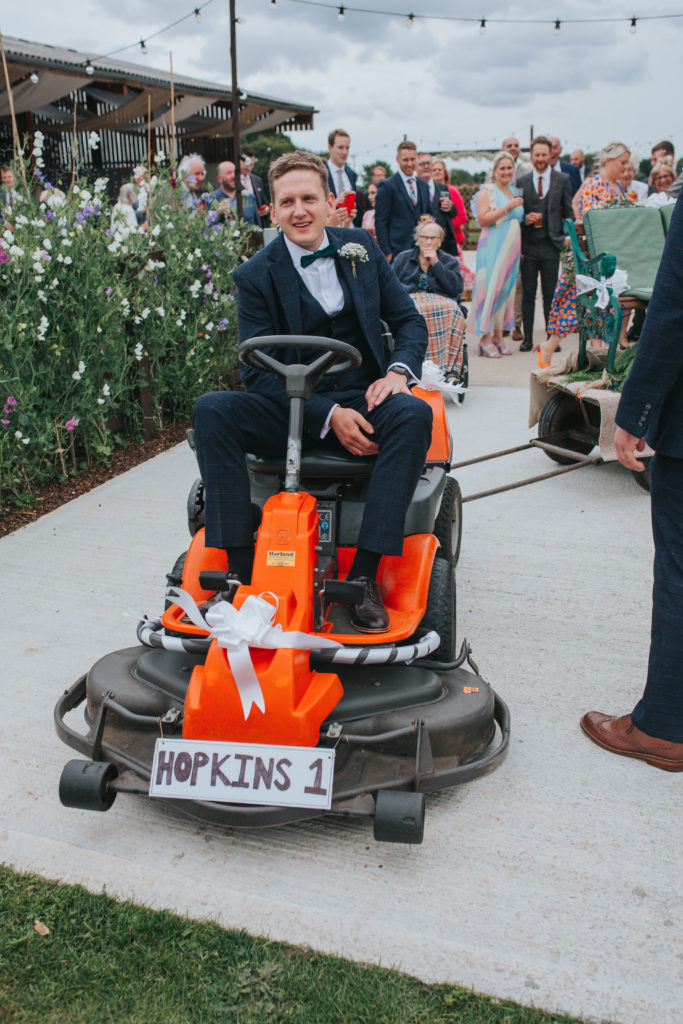 Groom Sam sits on a lawn mower towing a bench for bride Lucy to sit on.