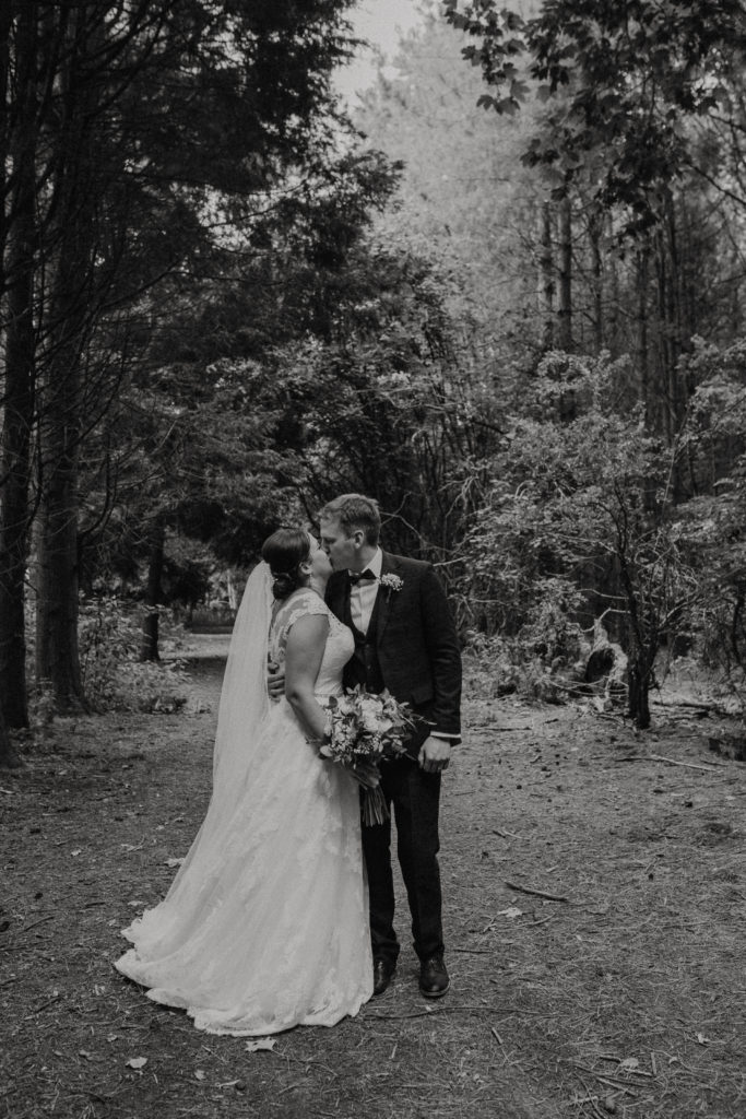 Black and white image. Lucy and Sam kiss in the woods.
