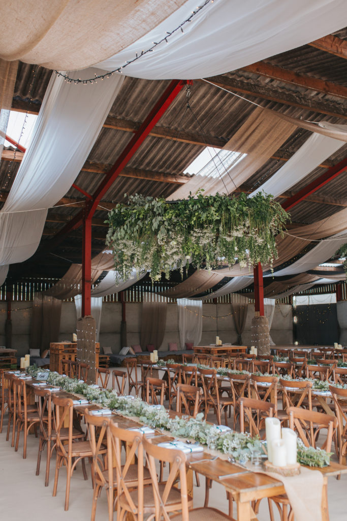Trestle tables positioned in long rows sit underneath large floral chandeliers.