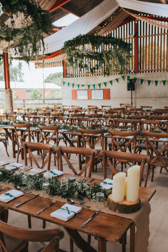 Wooden trestle tables dressed in foliage runners, silver cutlery and white napkins.