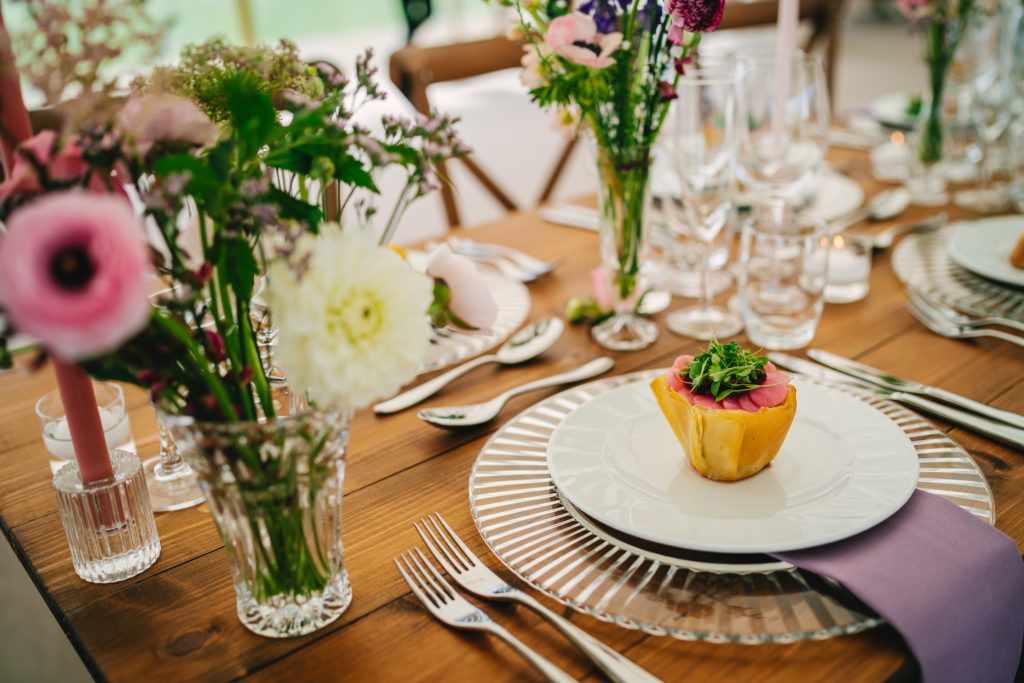 Close up shot of a starter on a wedding breakfast table. The table is dressed in bud vases of spring florals, glass ribbed edged charger plates, silver cutlery and mauve napkins.