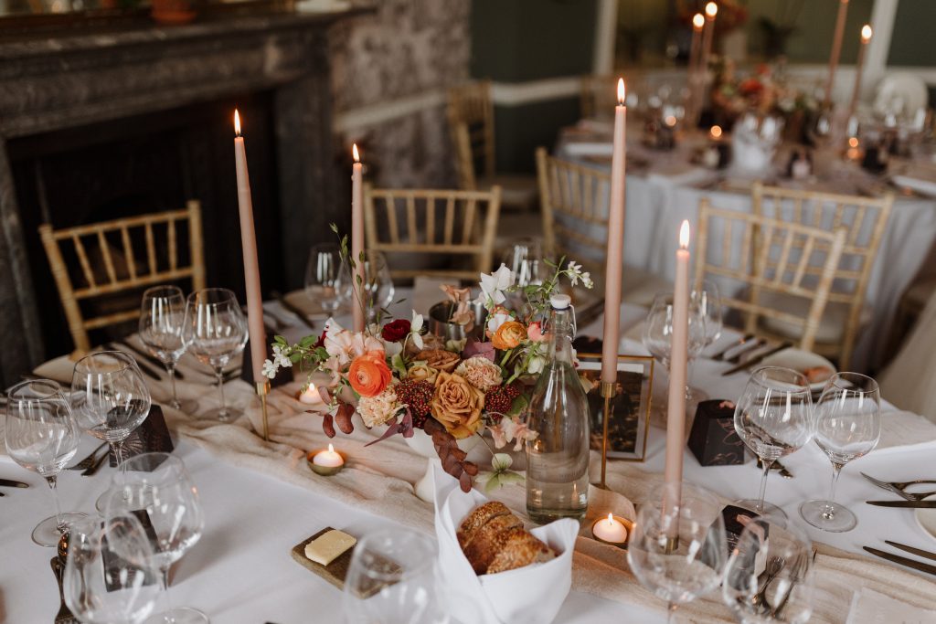 Round guest table in the dining room at Middleton Lodge. Set with gold tealights, parchment taper candles, autumnal blooms and white linen.