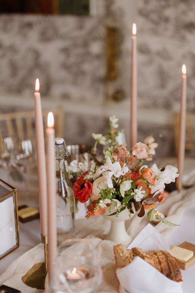 Close up of the beautiful wedding breakfast tables set for L&J's wedding at Middleton Lodge. A bowl of autumnal blooms sits on a taupe hand dyed muslin runner, surrounded by parchment taper candles.