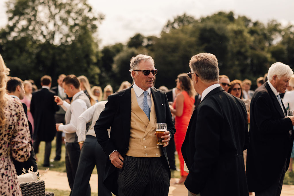 Marquee drinks reception held in a field. Guests can be seen mingling, catting and drinking pints of beer on a sunny day.